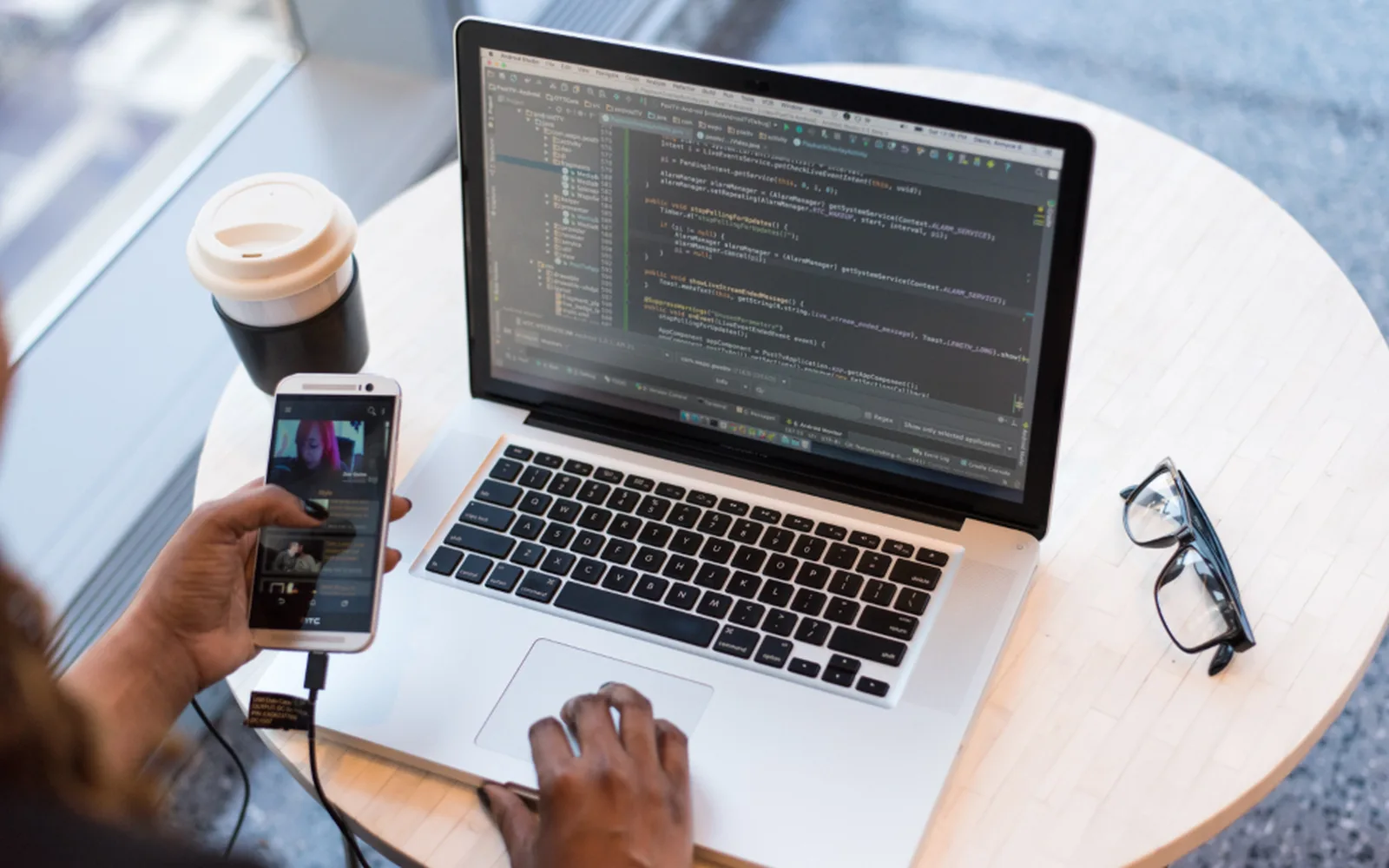 Hands on a laptop at a cafe table, with a phone and a coffee