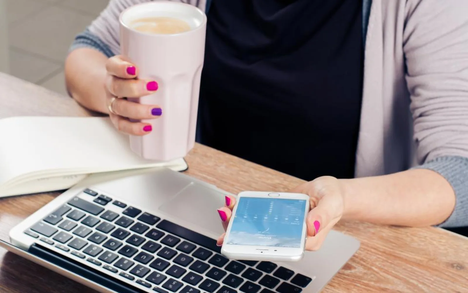 Coffee, a phone and a notebook beside a laptop